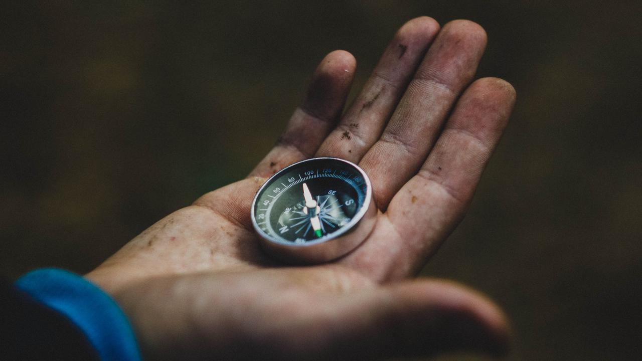 View of a white man's hand holding a compass.