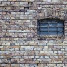 Old brick wall with a small, arched, cobweb-covered window.