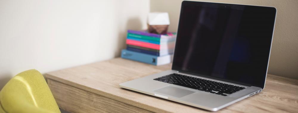 A laptop sites on a pale wood desk.