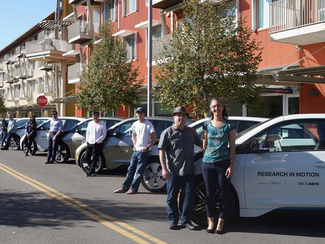 EV Project vechicles line a city street with drivers standing next to each car.