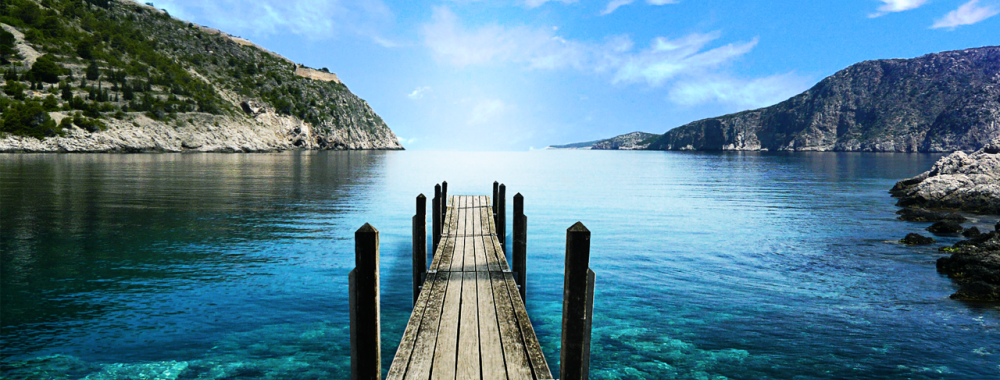 An old wooden dock extending out over the calm water of a bay on a sunny day.