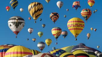 A photo of dozens of colorful hot air balloons filling a sunny blue sky.