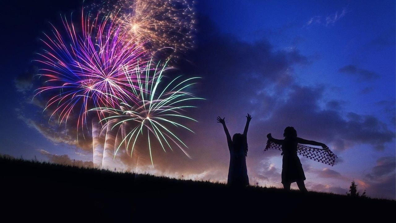 Fireworks exploding in the distance with two people silhouetted in the foreground.