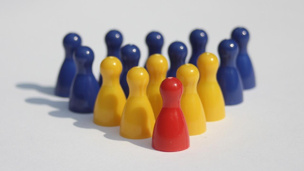 Stone figures arrayed in a pyramid shape, the single red one at the front, followed by a half dozen yellow figures, and then the remaining base in blue.