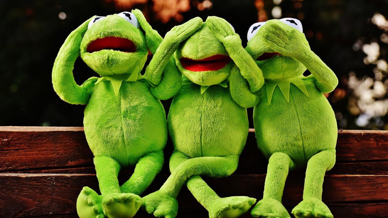 Three Kermit the Frog dolls sitting in the 'see no evil, hear no evil, speak no evil' pose.