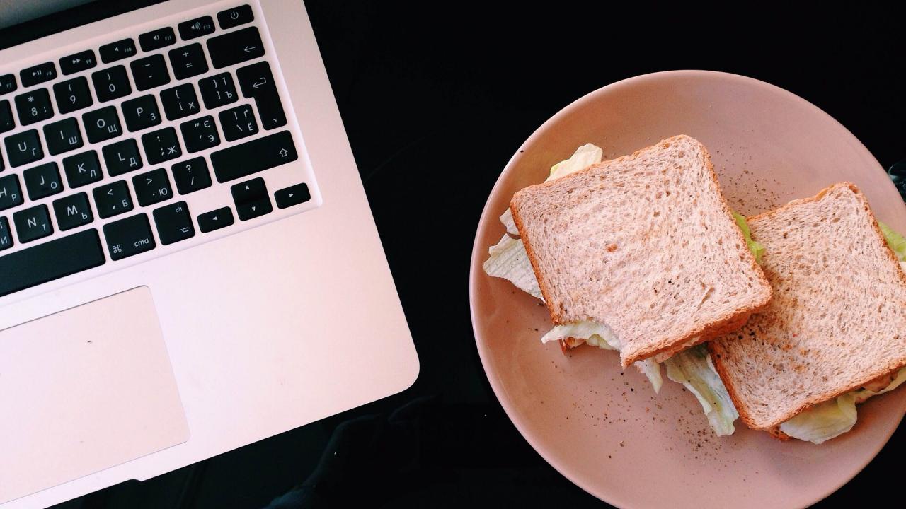A sandwich on a plate sits near a laptop.