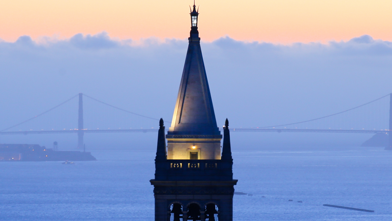 Sather Tower at dusk with the San Francisco Bay and the Golden Gate Bridge in the background.