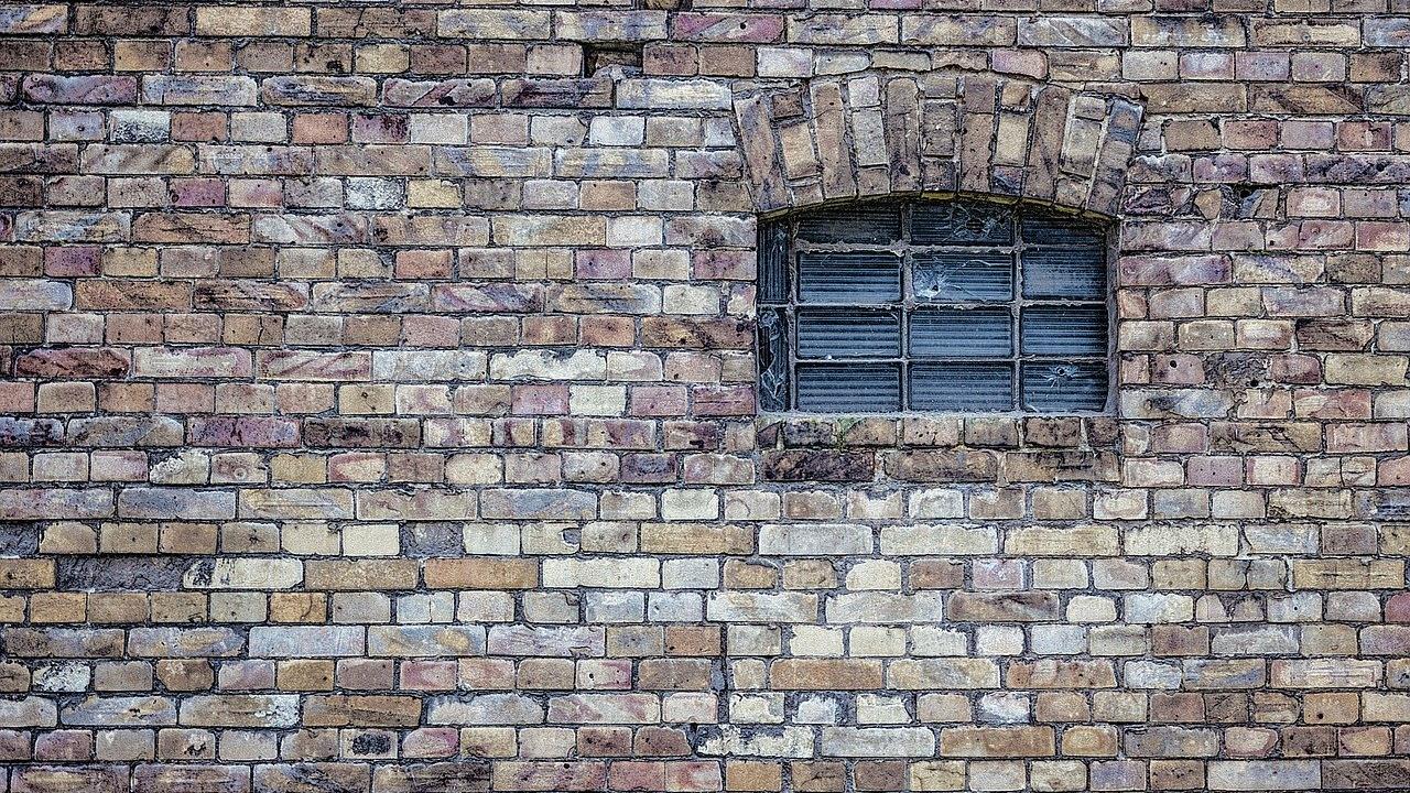Old brick wall with a small, arched, cobweb-covered window.