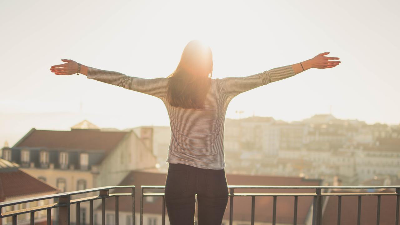 A woman on a balcony with her arms outstretched as she takes in the vista of the city below.