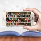 A man's hand holds a smartphone horizontally, its screen displaying a library of books.