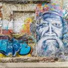 A colorful wall covered in graffiti art, tagged with lettering on the left and center, and the face of a man on the right. Photo by ShonEjai on Pixabay.