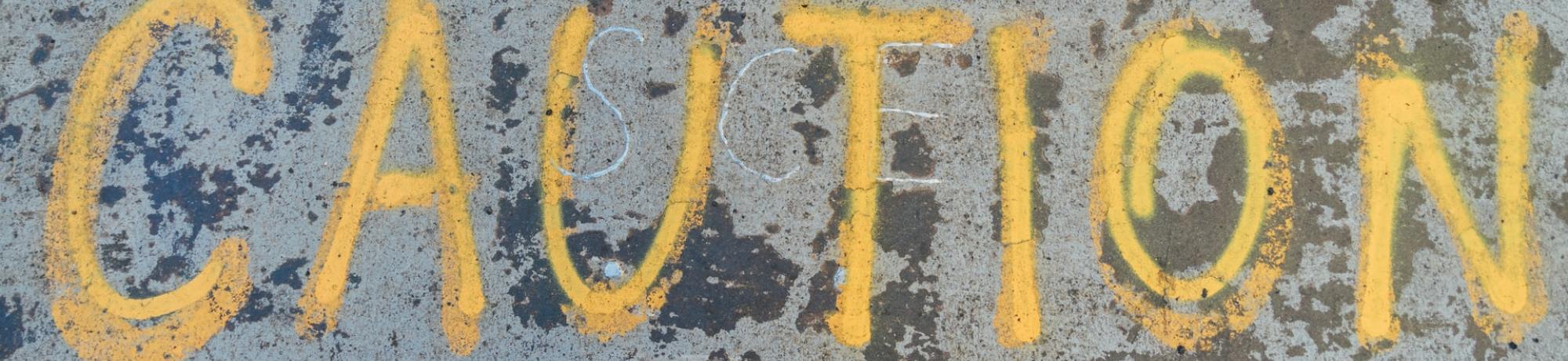 Photo by Goh Rhy Yan on Unsplash. The word 'Caution' is written on the ground.